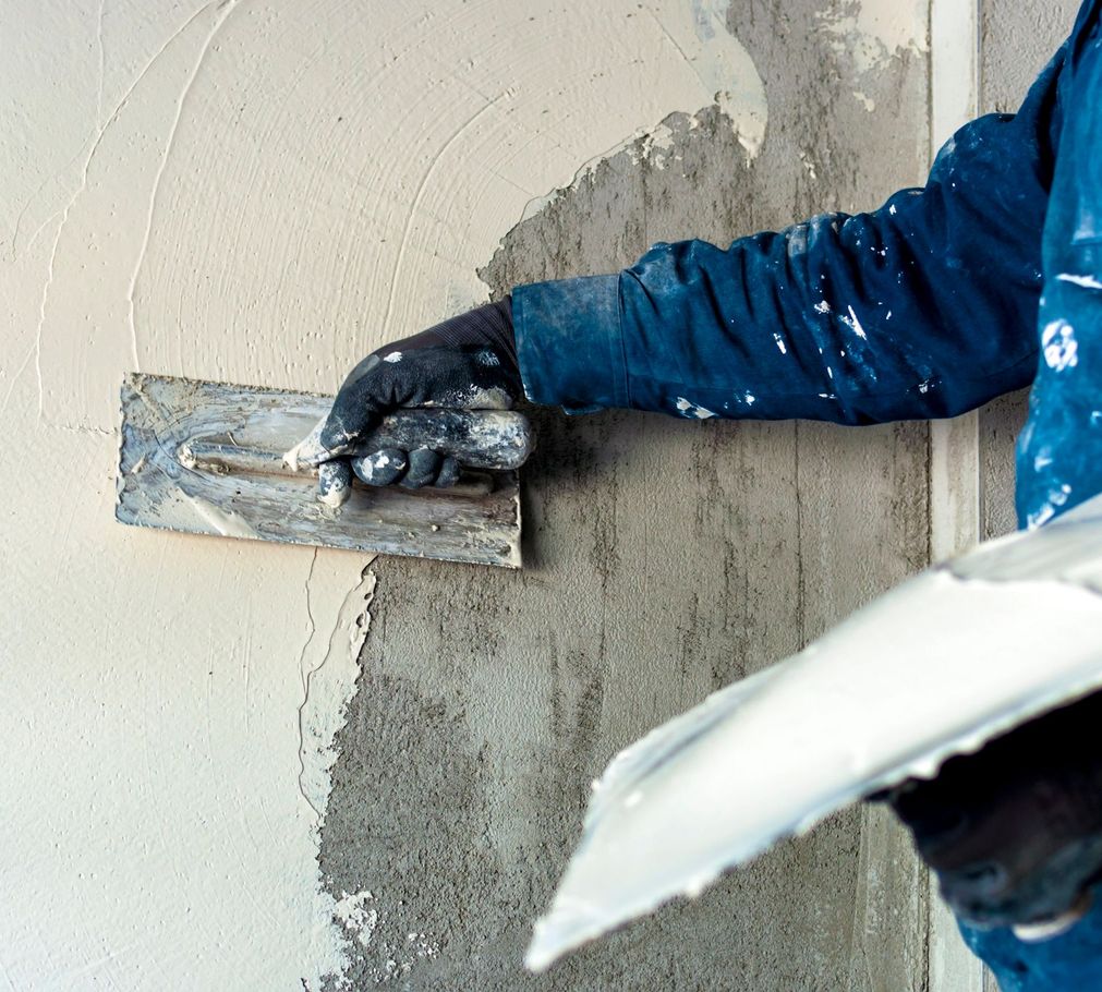 A man is holding a trowel and a bag of plaster.