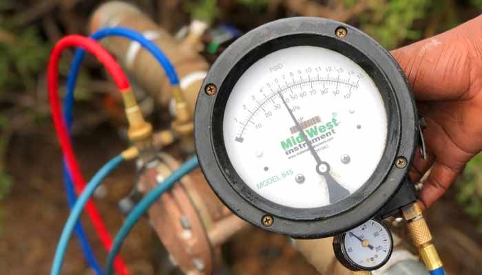 A person is holding a pressure gauge in front of a pipe.