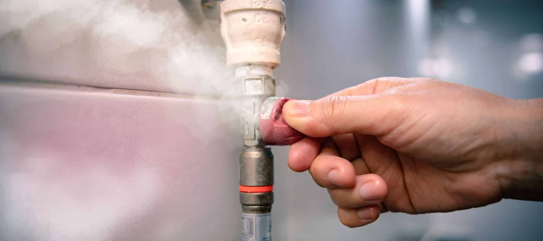 Hand turning a red valve on a steaming pipe.