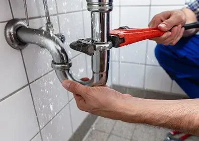 A plumber is fixing a pipe with a wrench in a bathroom.