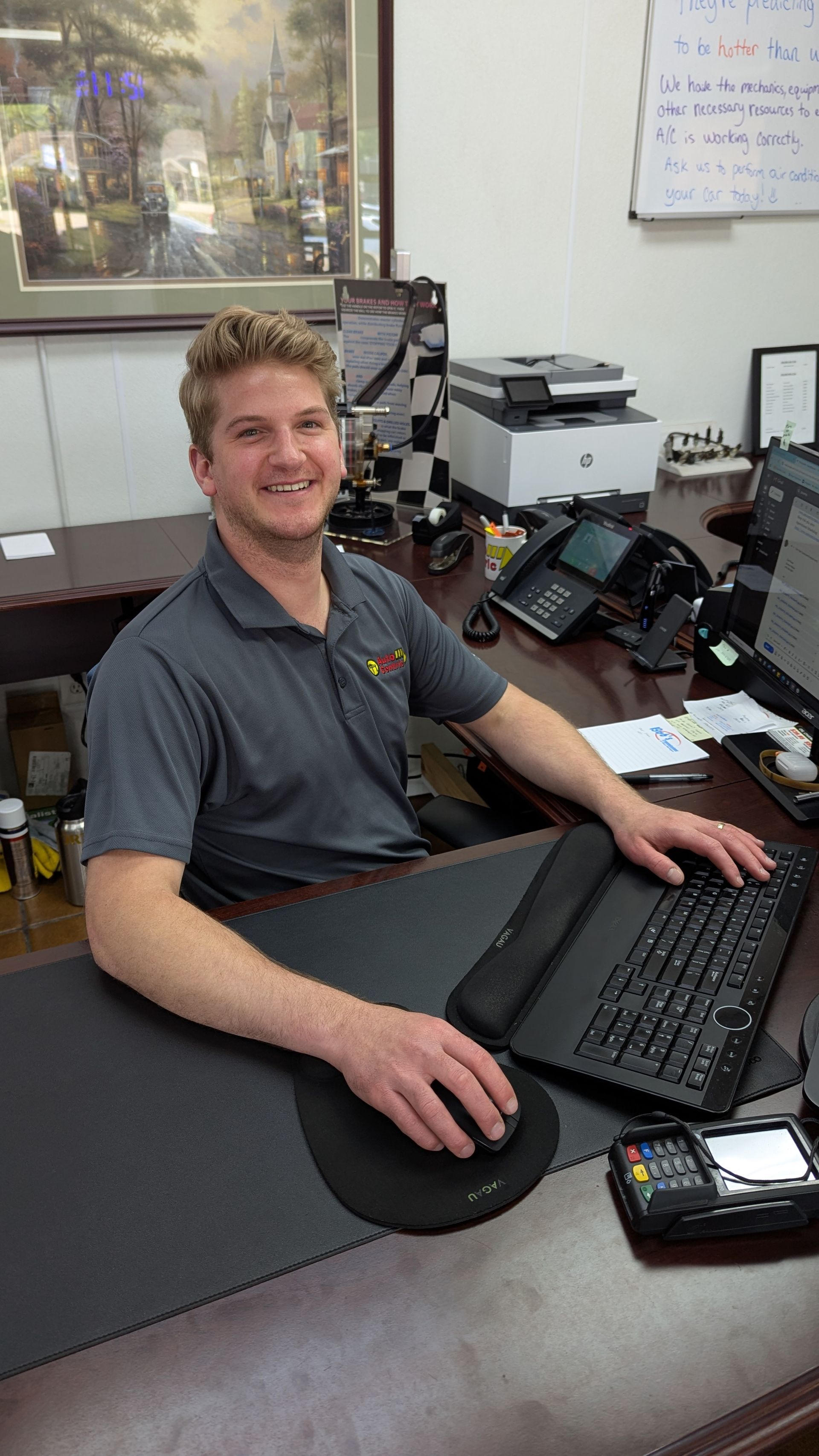 A smiling person sitting at a desk in an office, working at a computer with a keyboard and mouse.