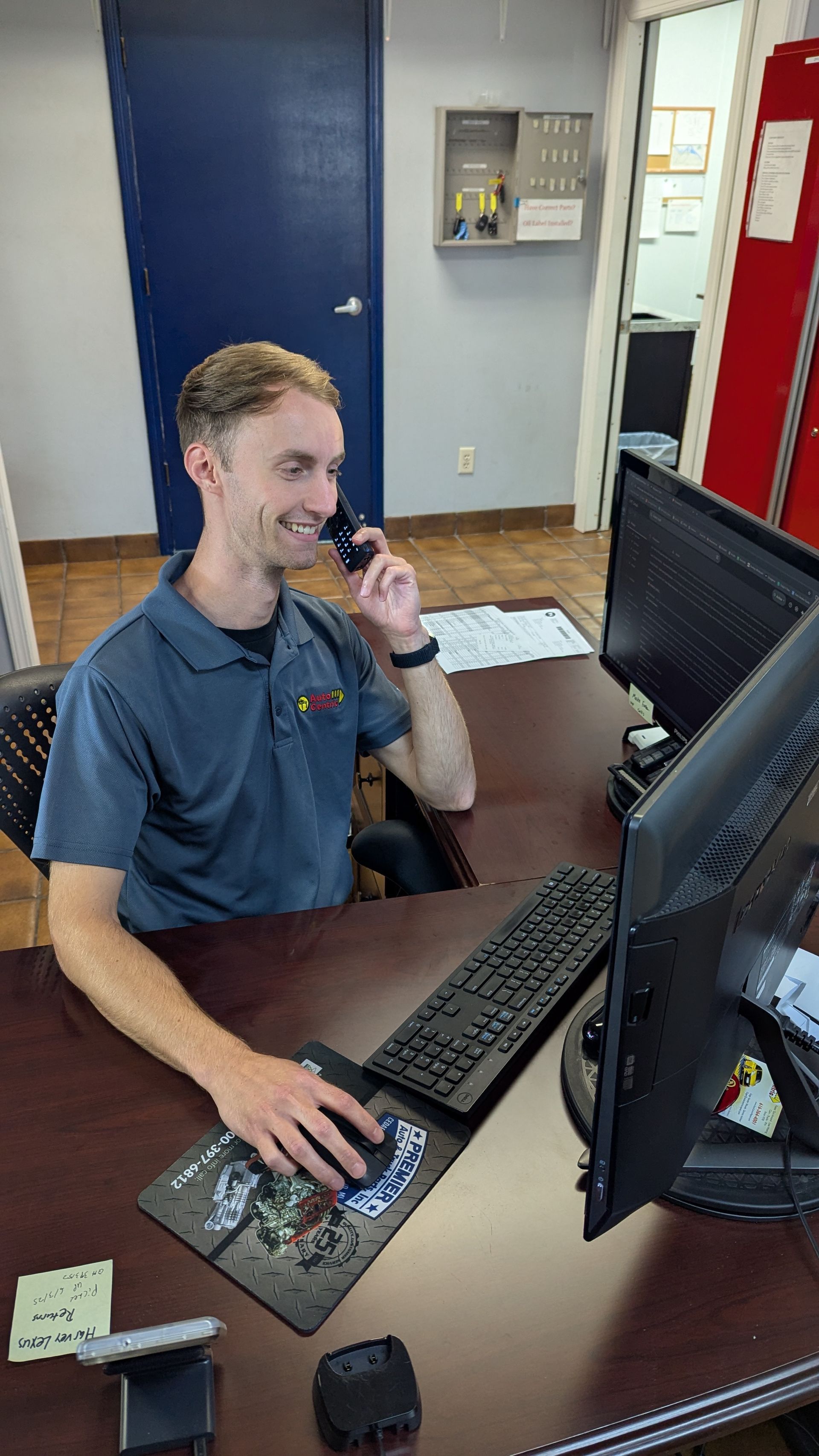 A person smiles while talking on a telephone and using a computer at a desk in an office.