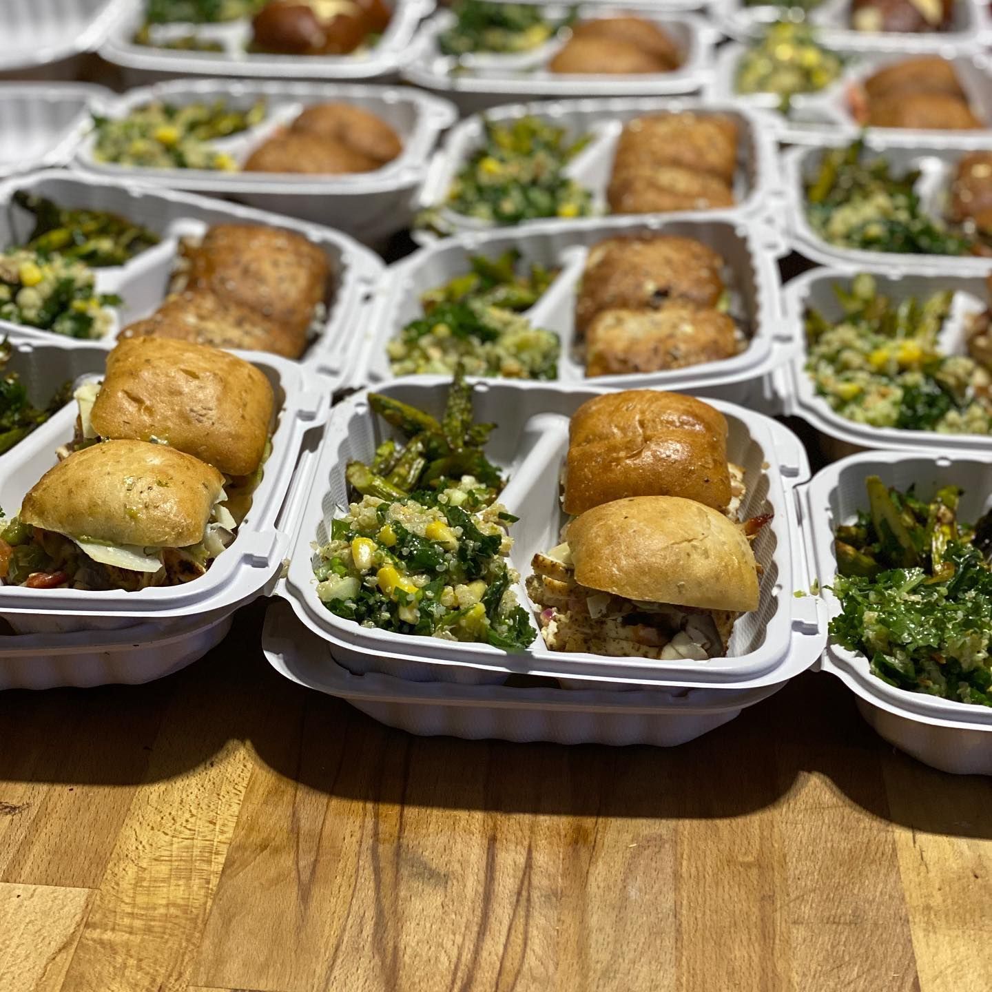 Takeout containers of sandwiches and chopped salad arranged on a wooden table