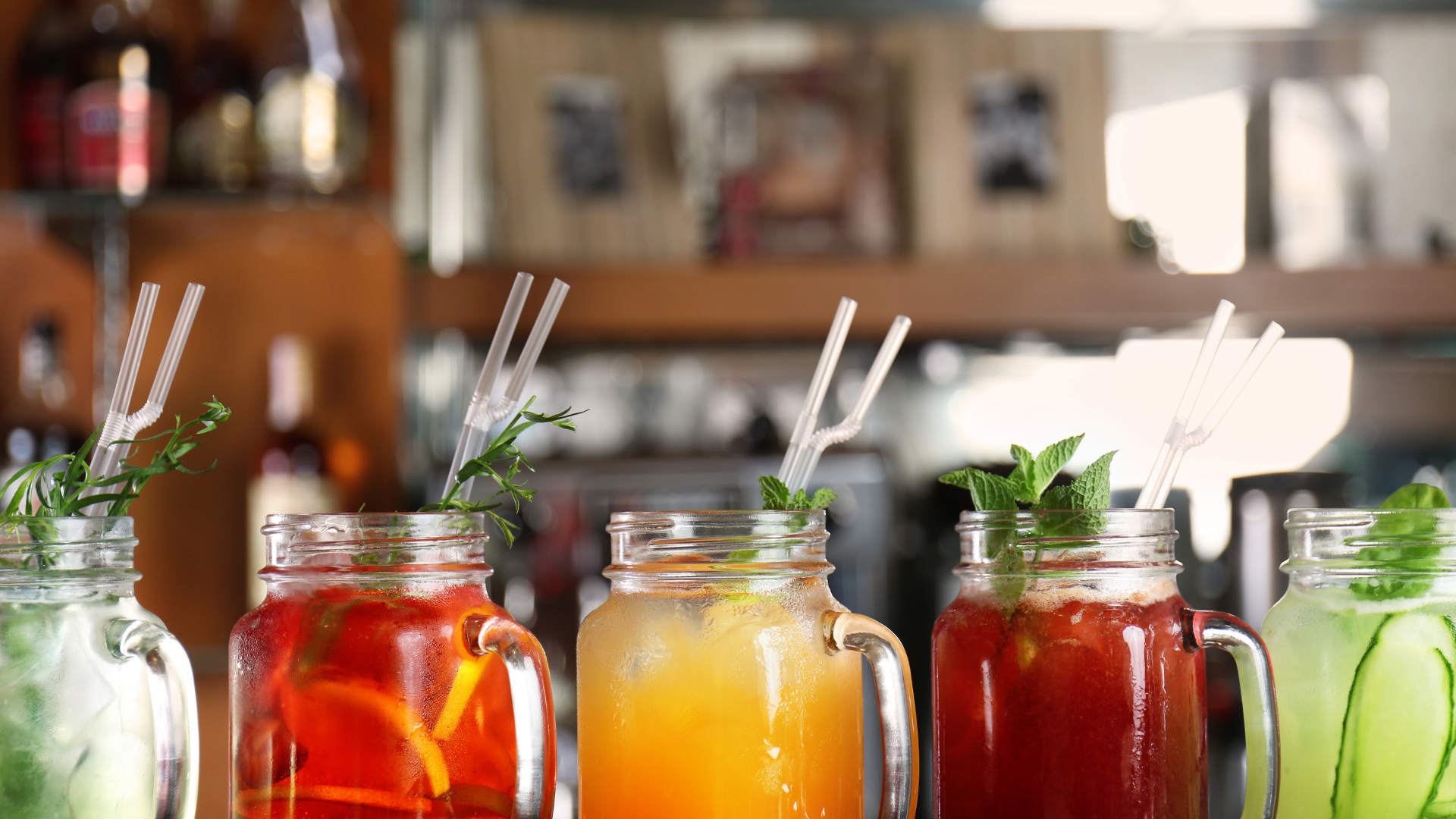 Assorted colorful jar drinks with straws on a counter in a café setting