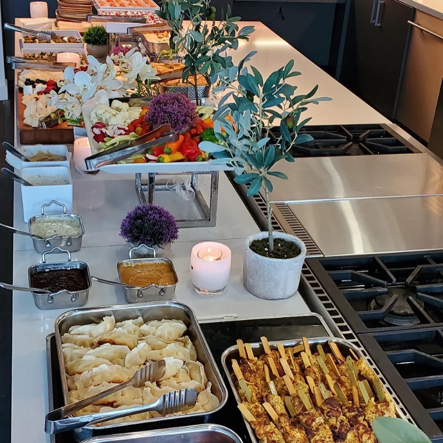 Buffet spread with pastries, fruit, dips, and grilled skewers on a modern kitchen island