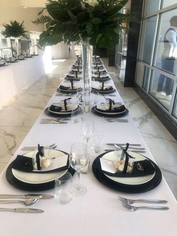 Long banquet table set with black-and-white place settings and lush floral centerpieces in a bright room
