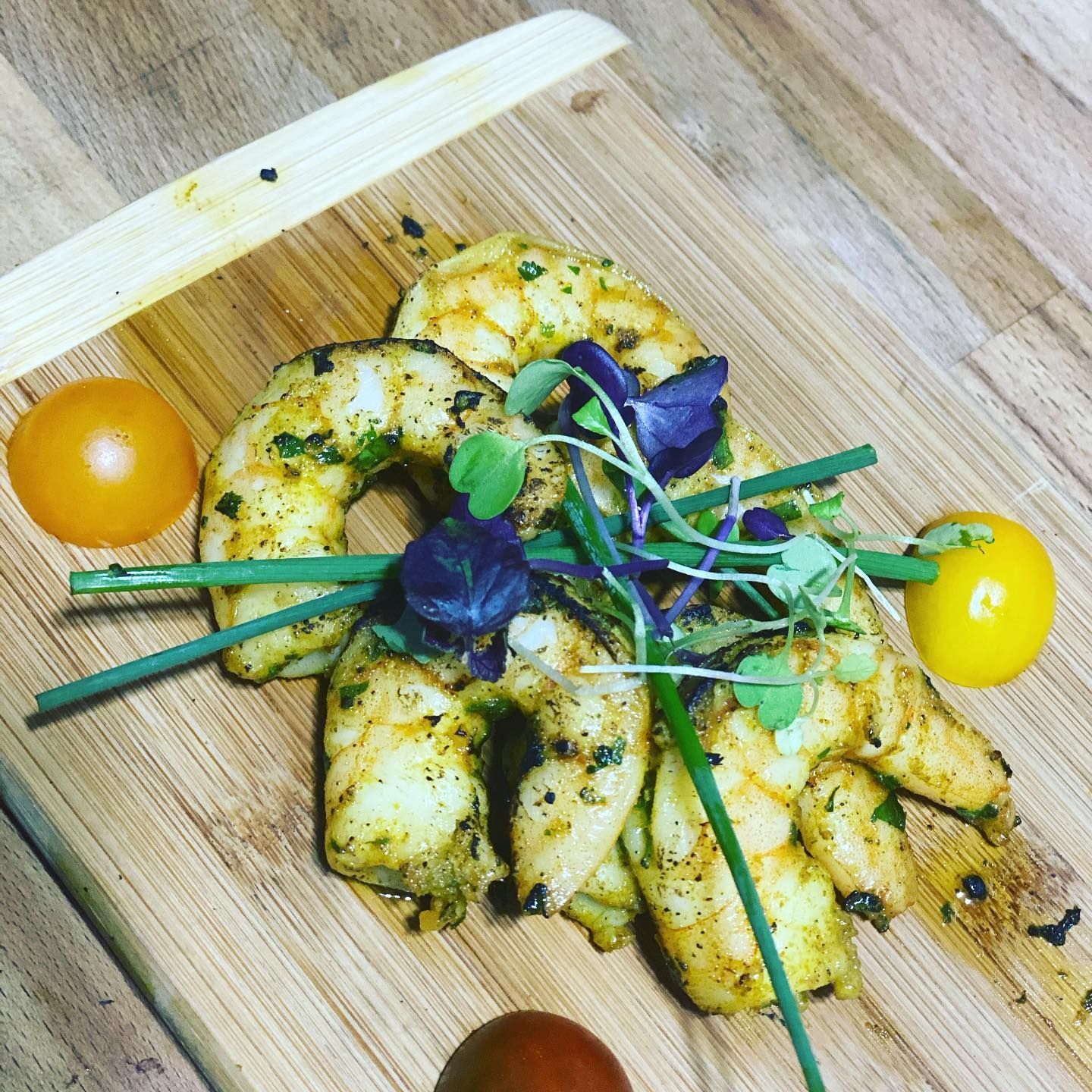 Herb-seasoned roasted potatoes on a wooden board with microgreens and yellow cherry tomatoes