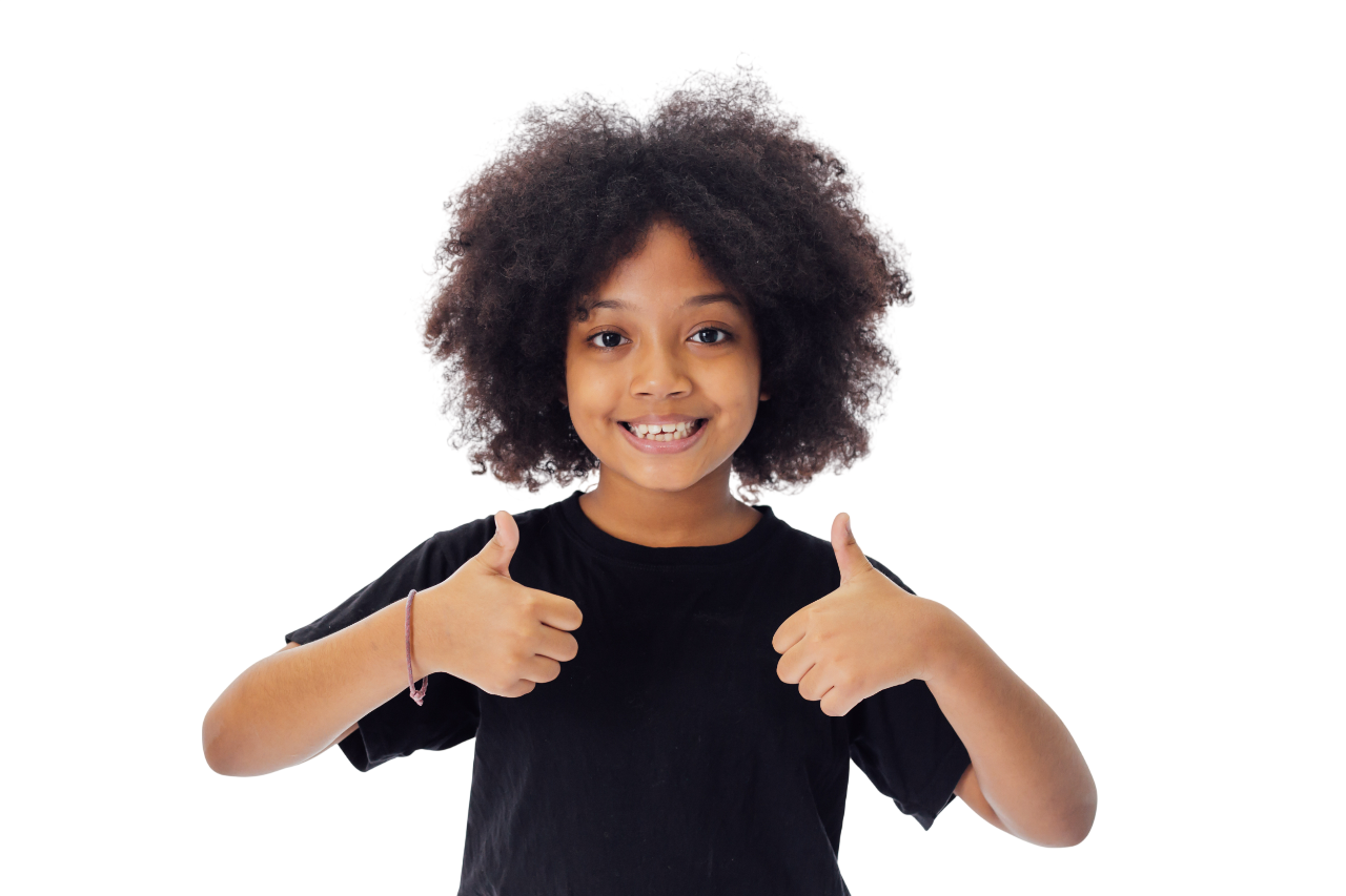 Smiling child with curly brown hair, wearing a striped shirt and blue pants, sitting and laughing.