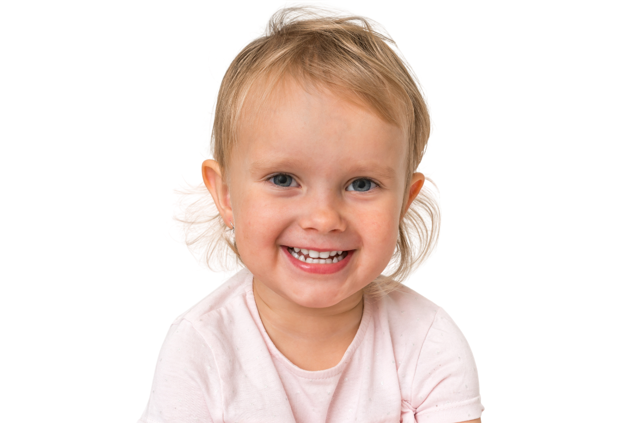 Smiling child with curly hair wearing a white sweater, looking upwards.