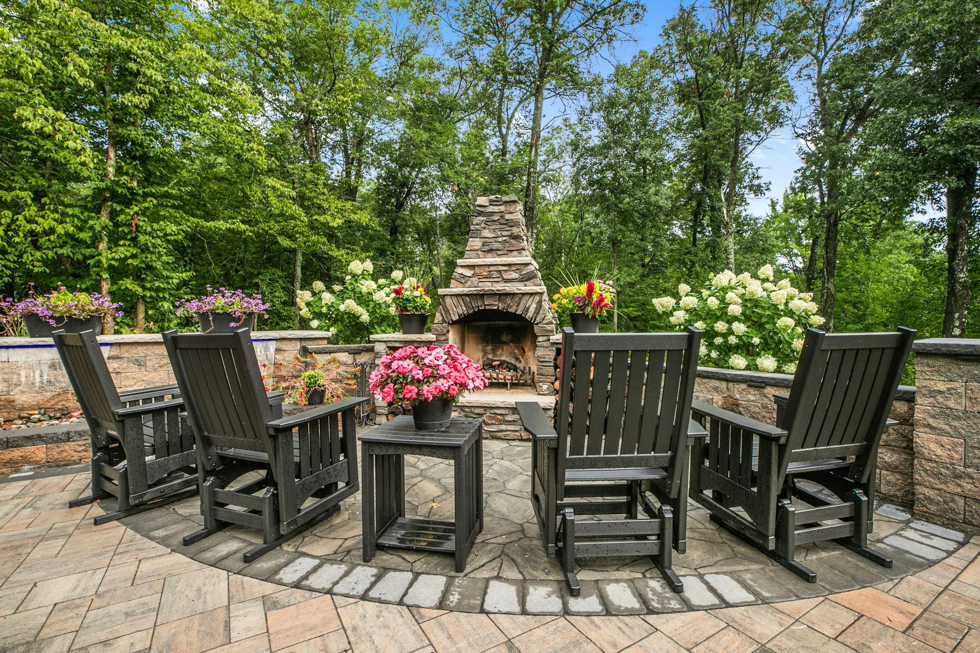 Backyard patio with stone paving, outdoor seating, and a tan house surrounded by trees