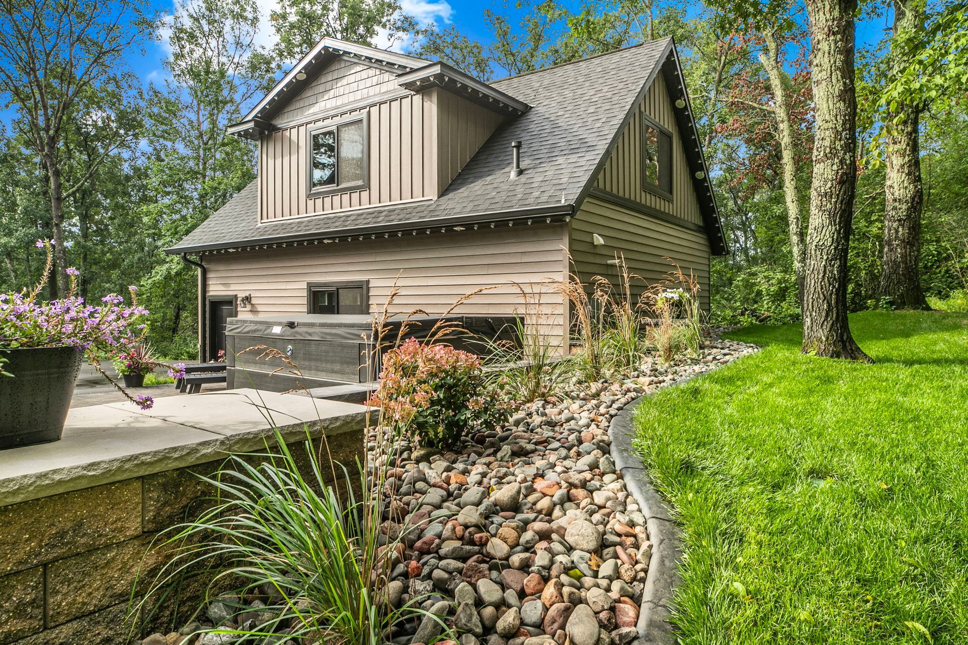 Suburban house with stone-lined driveway, green lawn, and trees in a sunny yard