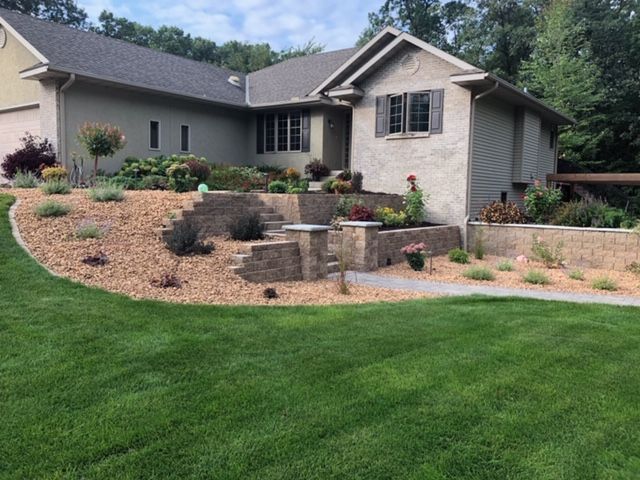 Single-story house with landscaped front yard, stone retaining wall, and green lawn