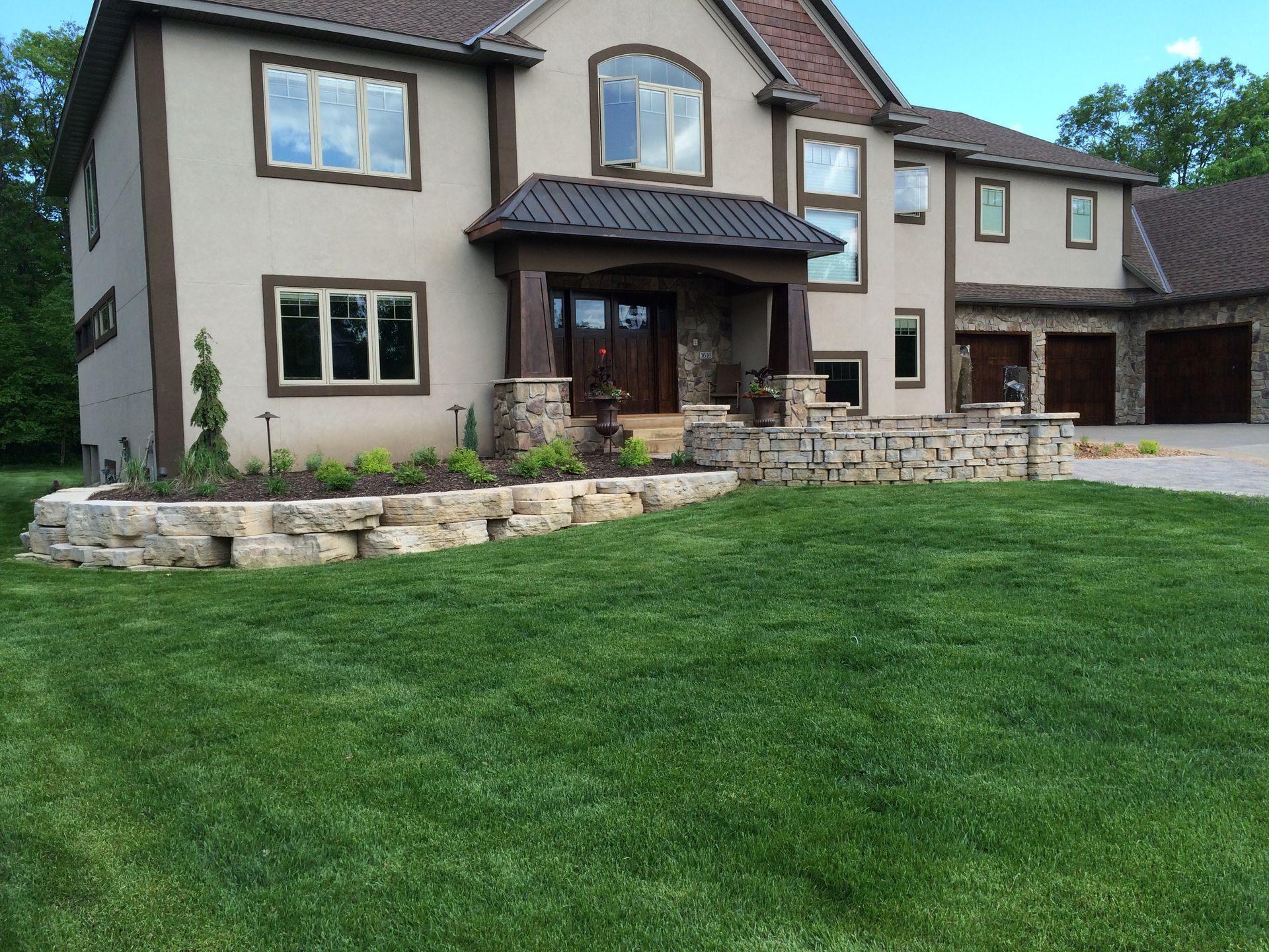 Large beige suburban house with stone accents and a wide green lawn