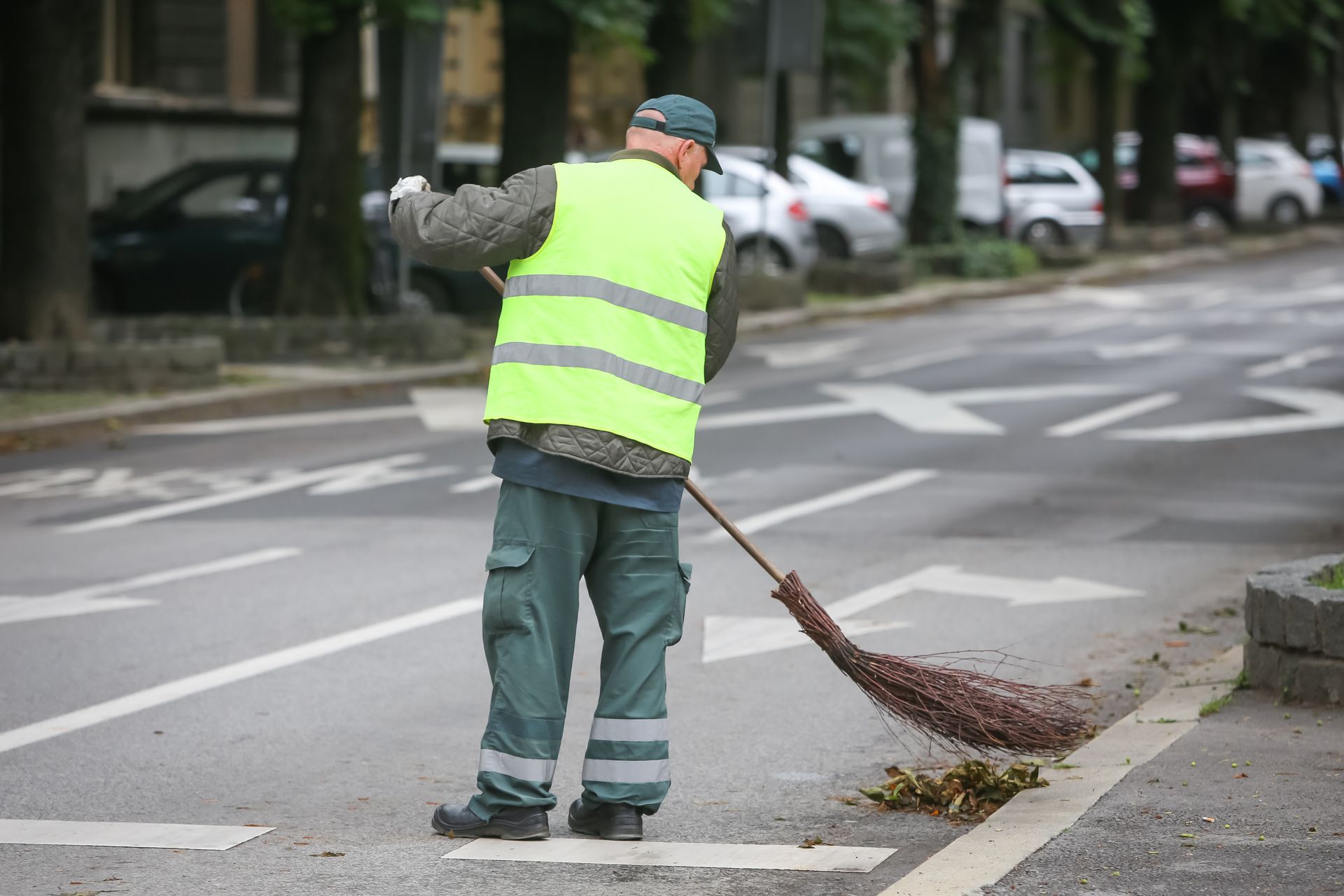 Road worker in a neon vest sweeping debris from the street curb