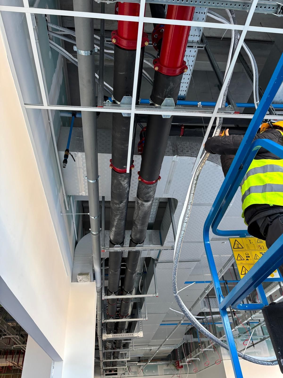 Un uomo è in piedi su una scala in un edificio con dei tubi che pendono dal soffitto.