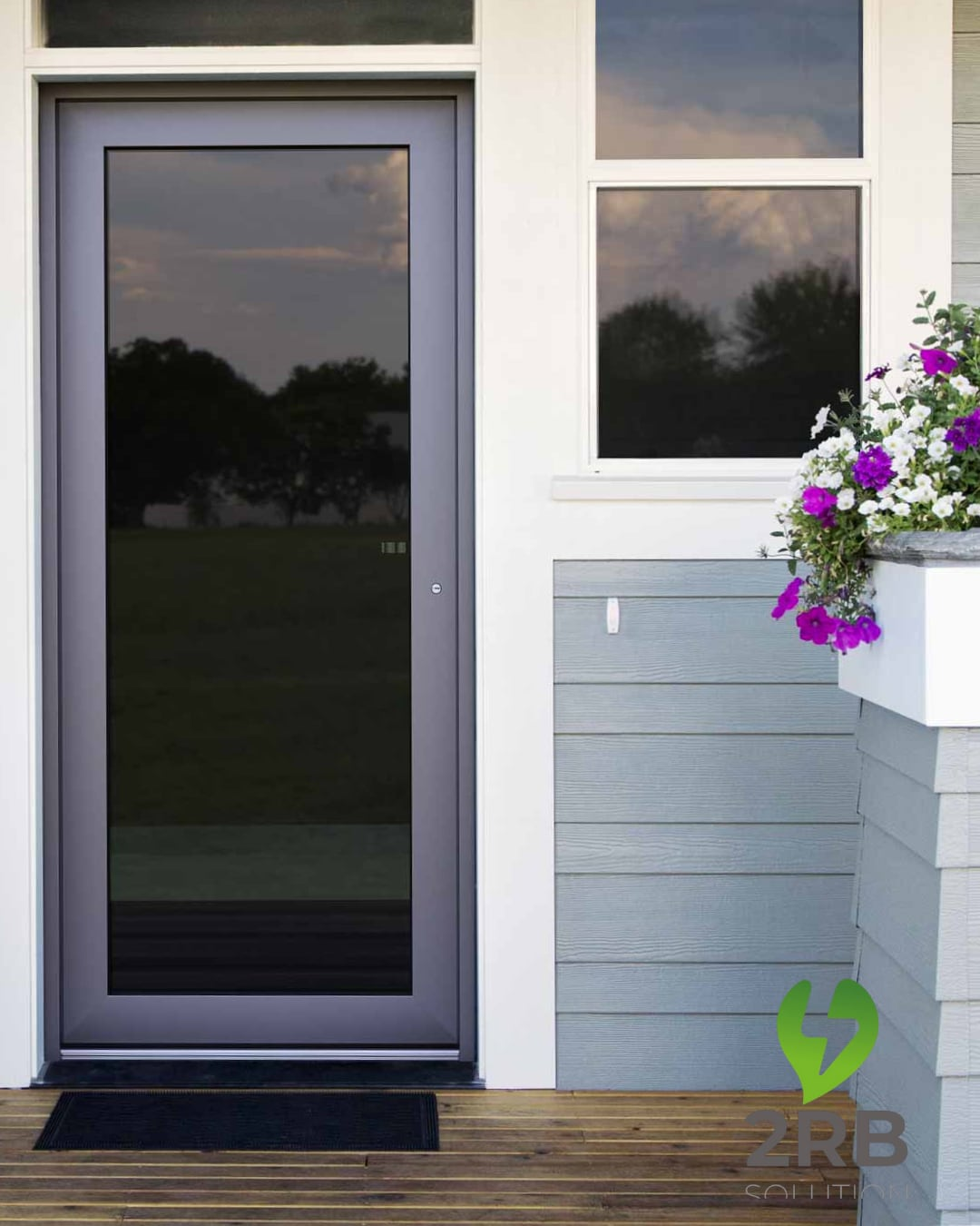 Porta grigia con grande finestra, zerbino nero, rifiniture bianche e fiori sul portico.