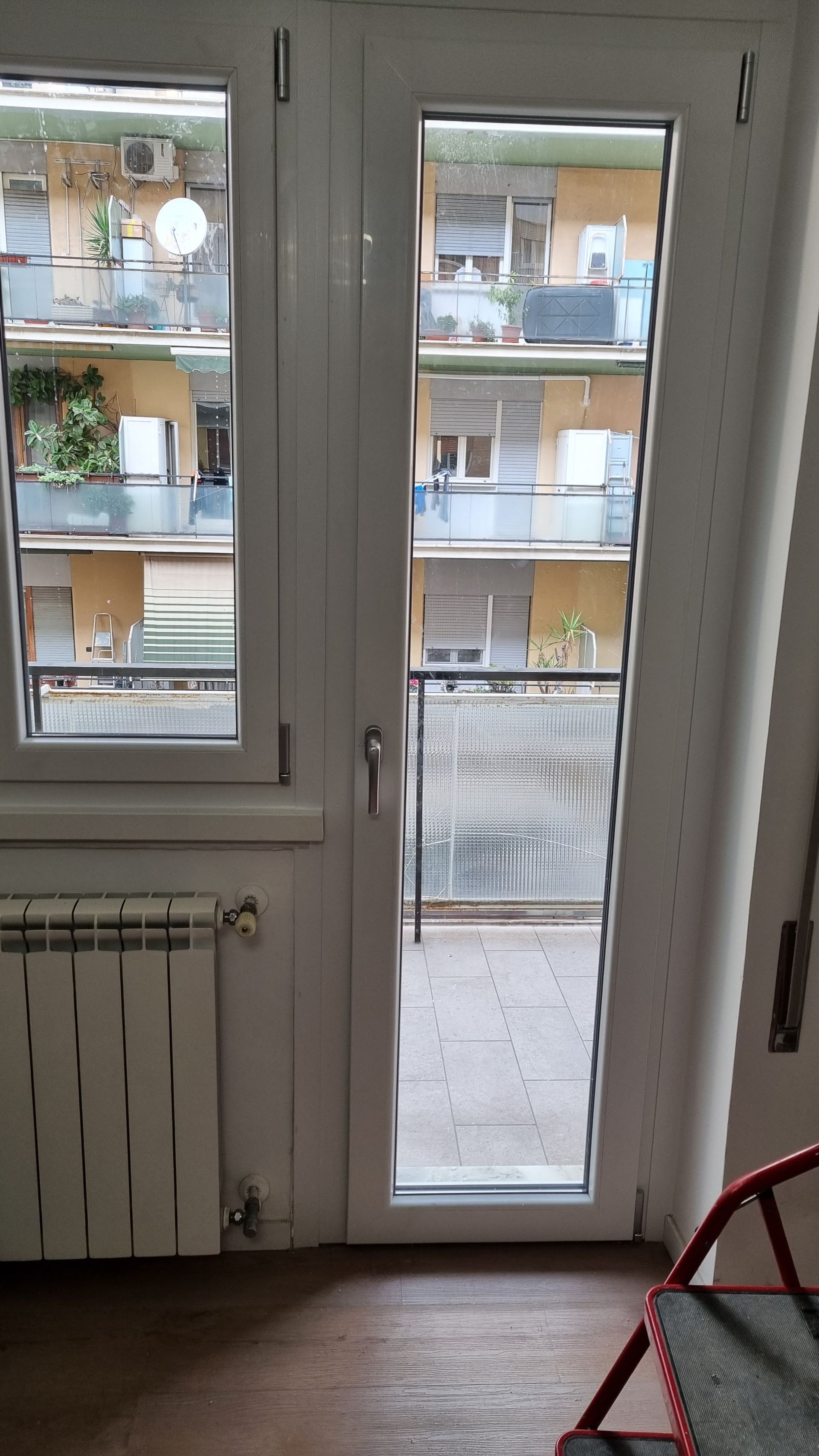 Porta e finestra bianche che si aprono su un balcone con edifici dall'altra parte della strada.