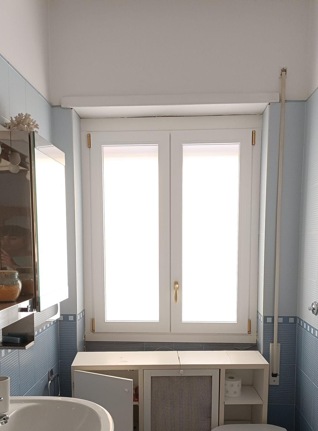 Bagno con pareti piastrellate blu, finestra bianca, mobiletto e lavandino.