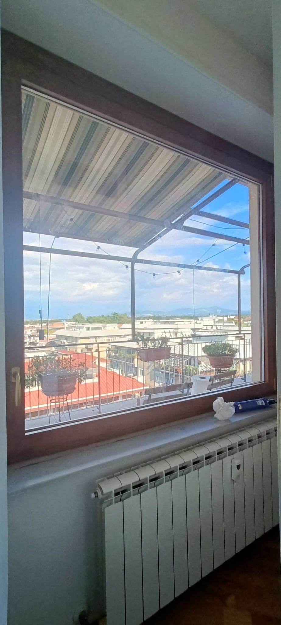 Vista attraverso una finestra di una città con tetti e cielo azzurro; termosifone bianco.