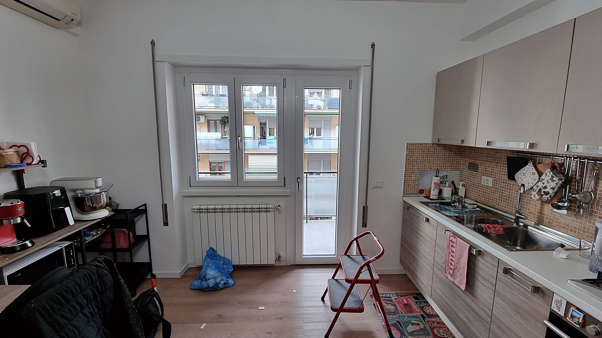 Interno della cucina con finestra, banconi e sgabello rosso.