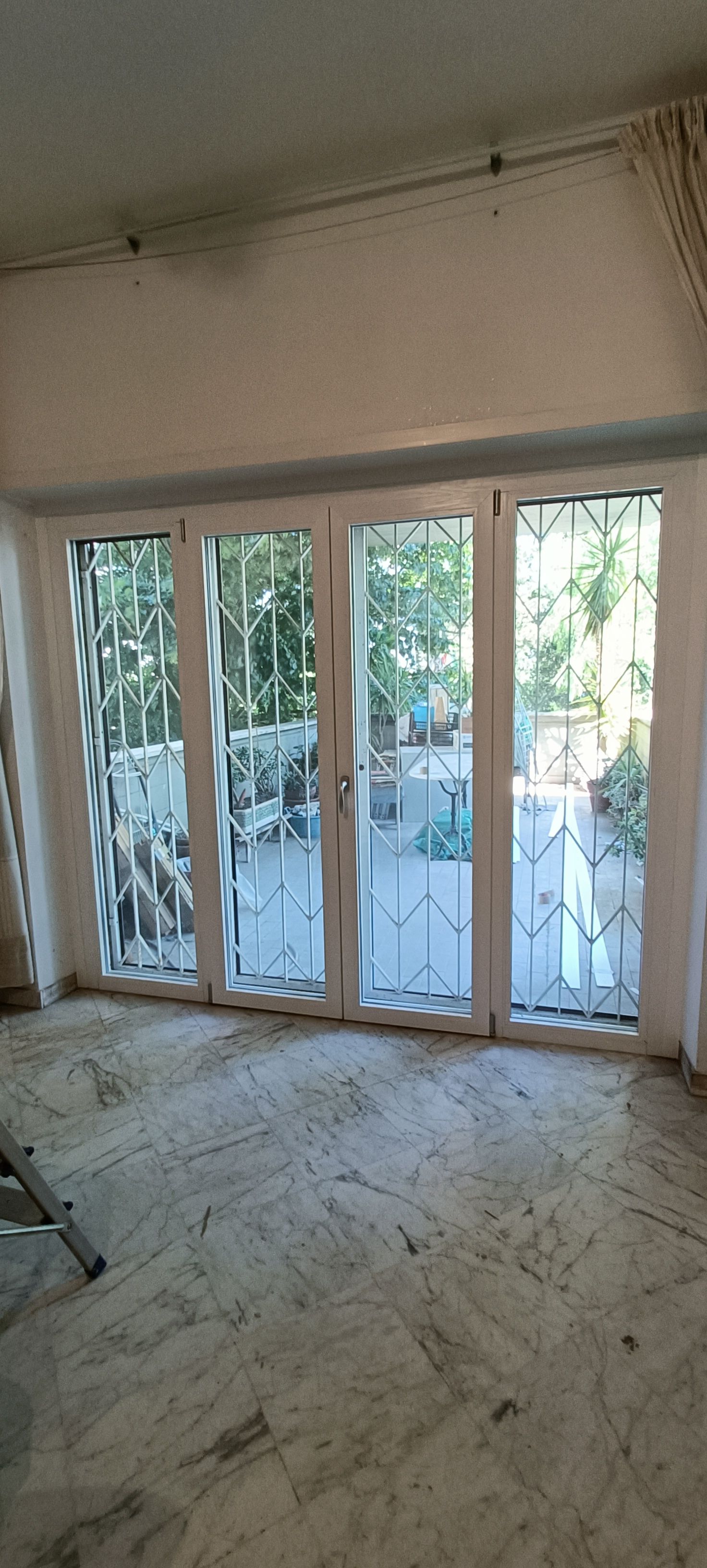 Stanza con porte con cornice bianca e grate di sicurezza, vista sul cortile. Pavimento vecchio e usurato.