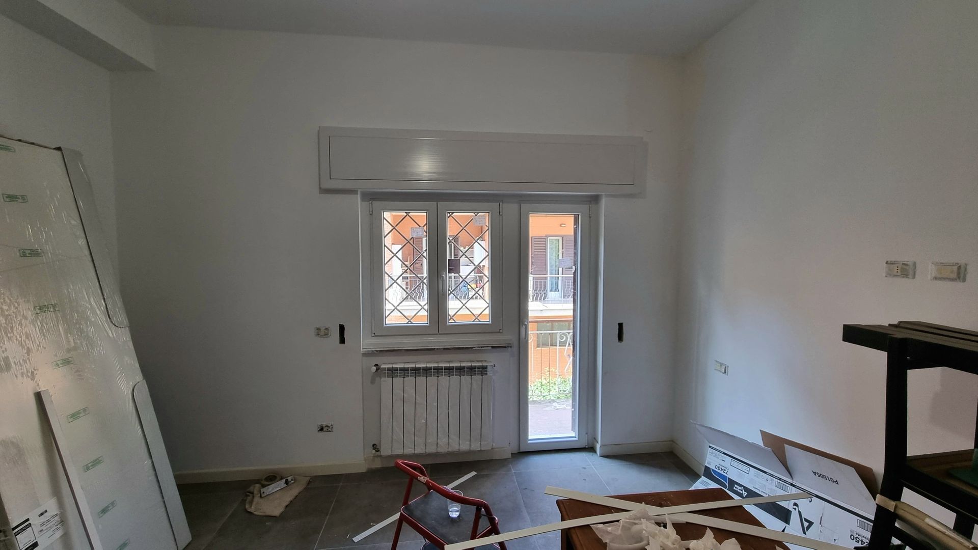 Stanza vuota con finestra e aria condizionata, materiali da costruzione e un piccolo termosifone.