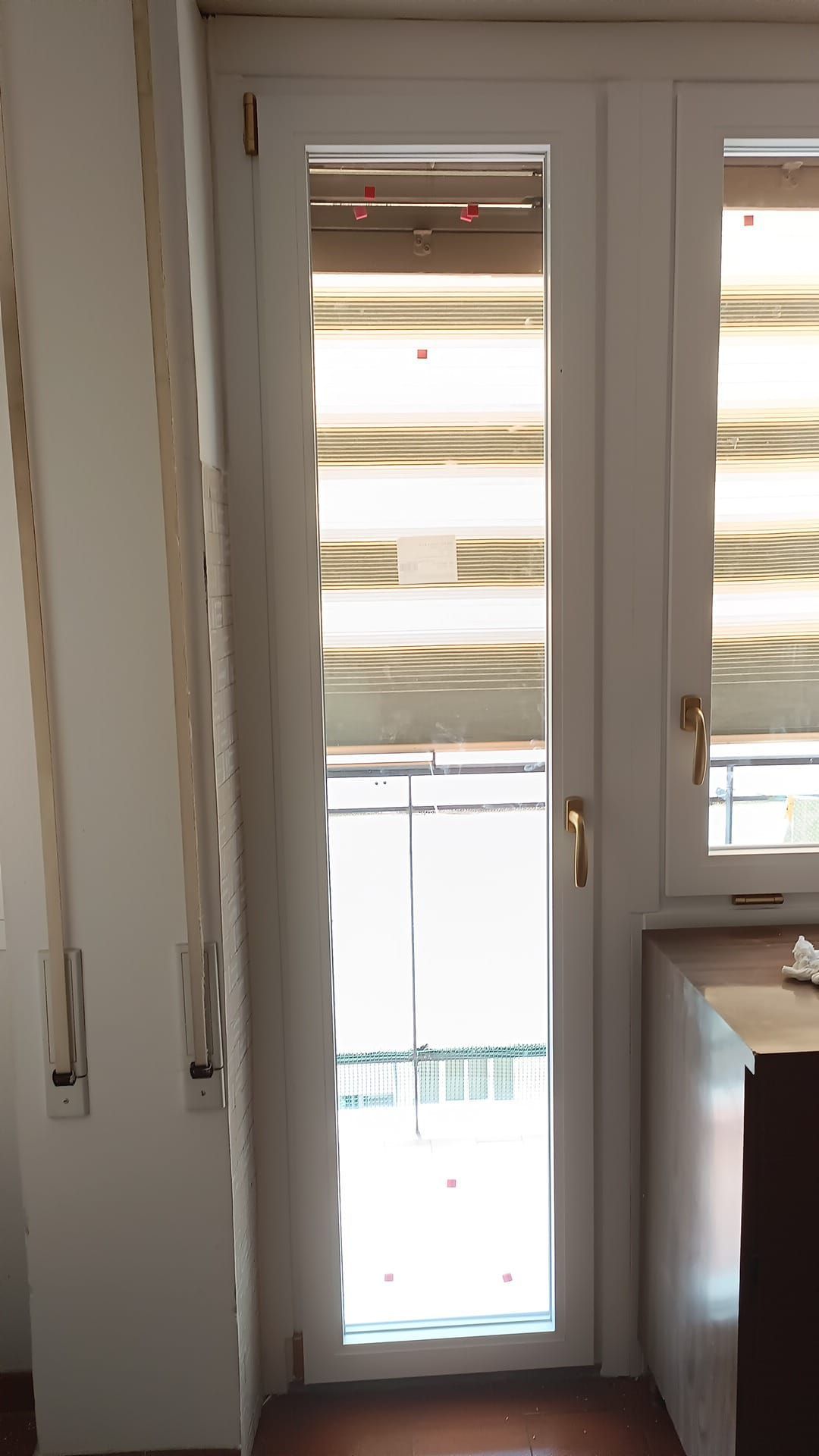 Porta bianca con finestra aperta, luce del sole che filtra, persiane parzialmente abbassate.