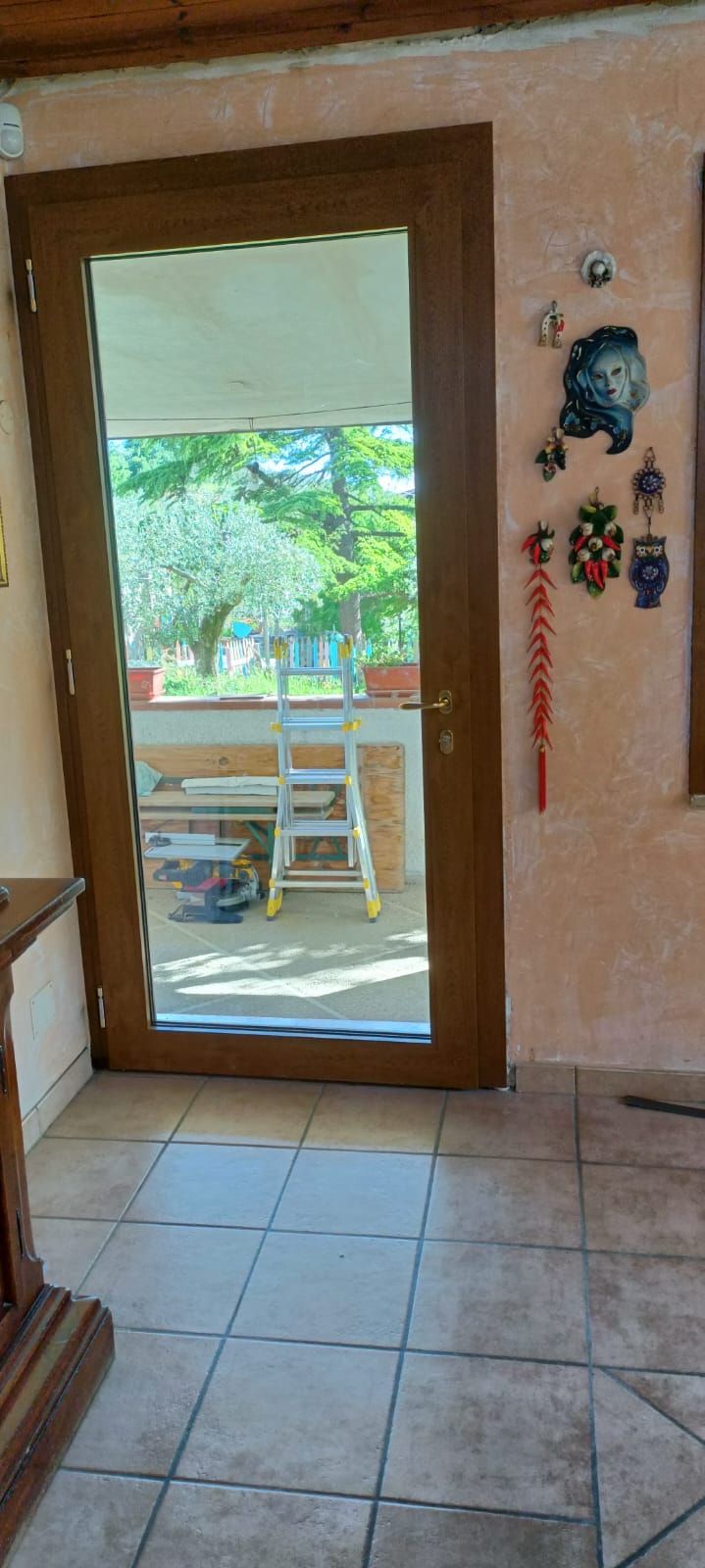 Una porta a vetri con telaio in legno in una stanza con pavimento piastrellato, una scala visibile all'esterno.