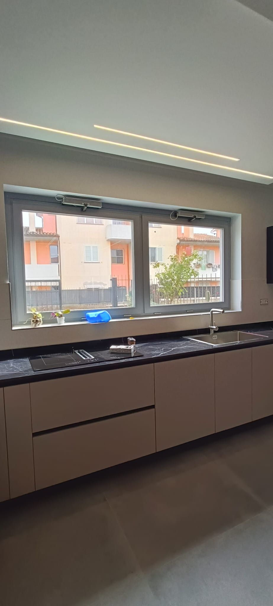 Una cucina con mobili chiari, piano di lavoro nero e una finestra che si affaccia su un edificio.