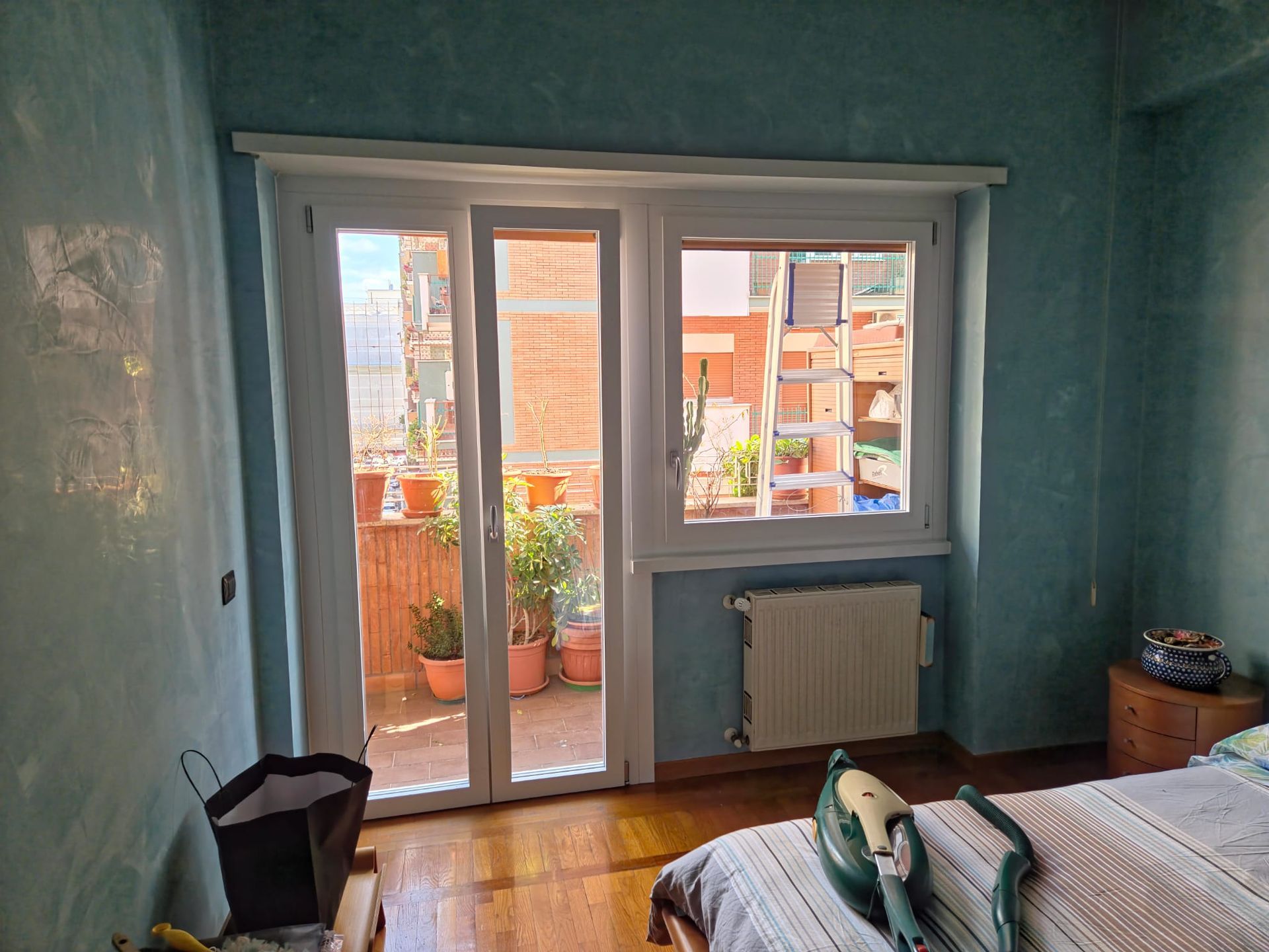 Camera da letto con balcone e vista: porte e finestre con cornice bianca, pareti blu, pavimento in legno, letto.