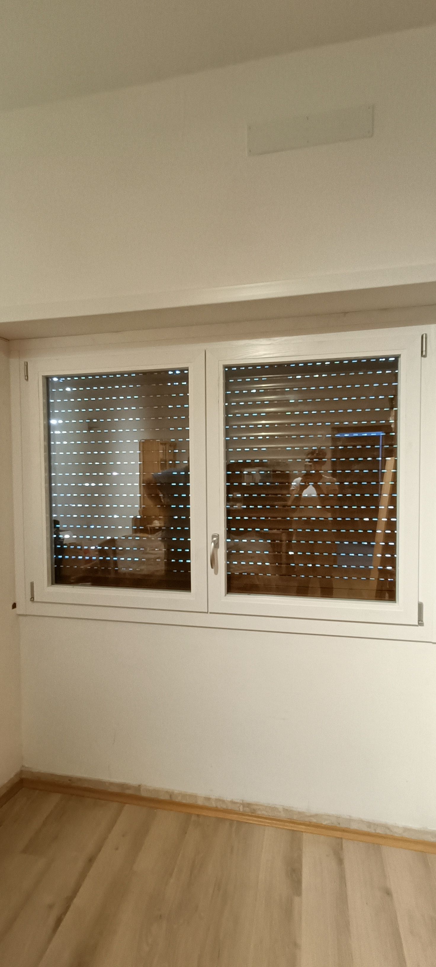 Una finestra con le persiane chiuse in una stanza con pavimenti in legno e pareti bianche.