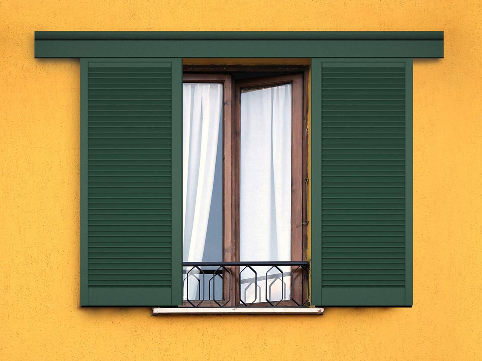 Le persiane verdi incorniciano una finestra con tende bianche su un edificio giallo.