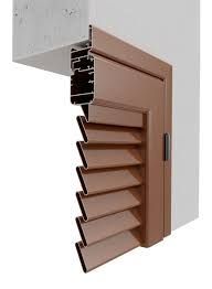 Pannello di ventilazione con persiane in metallo marrone installato su una parete bianca, con una sezione in cemento soprastante.