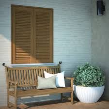 Panca in legno con cuscini, pianta in vaso e finestra con persiane contro una parete strutturata.