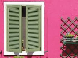 Persiane verdi su una finestra su una parete rosa, con un portavasi decorativo sulla destra.