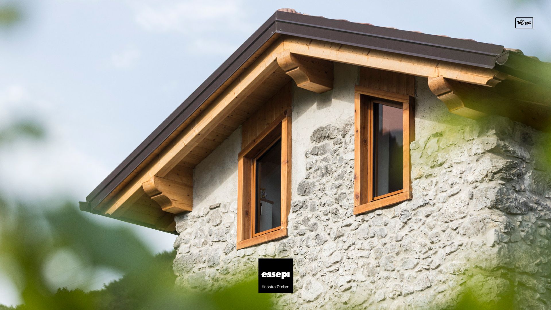 Edificio in pietra con finestre e tetto rifiniti in legno; situato all'esterno con vegetazione.