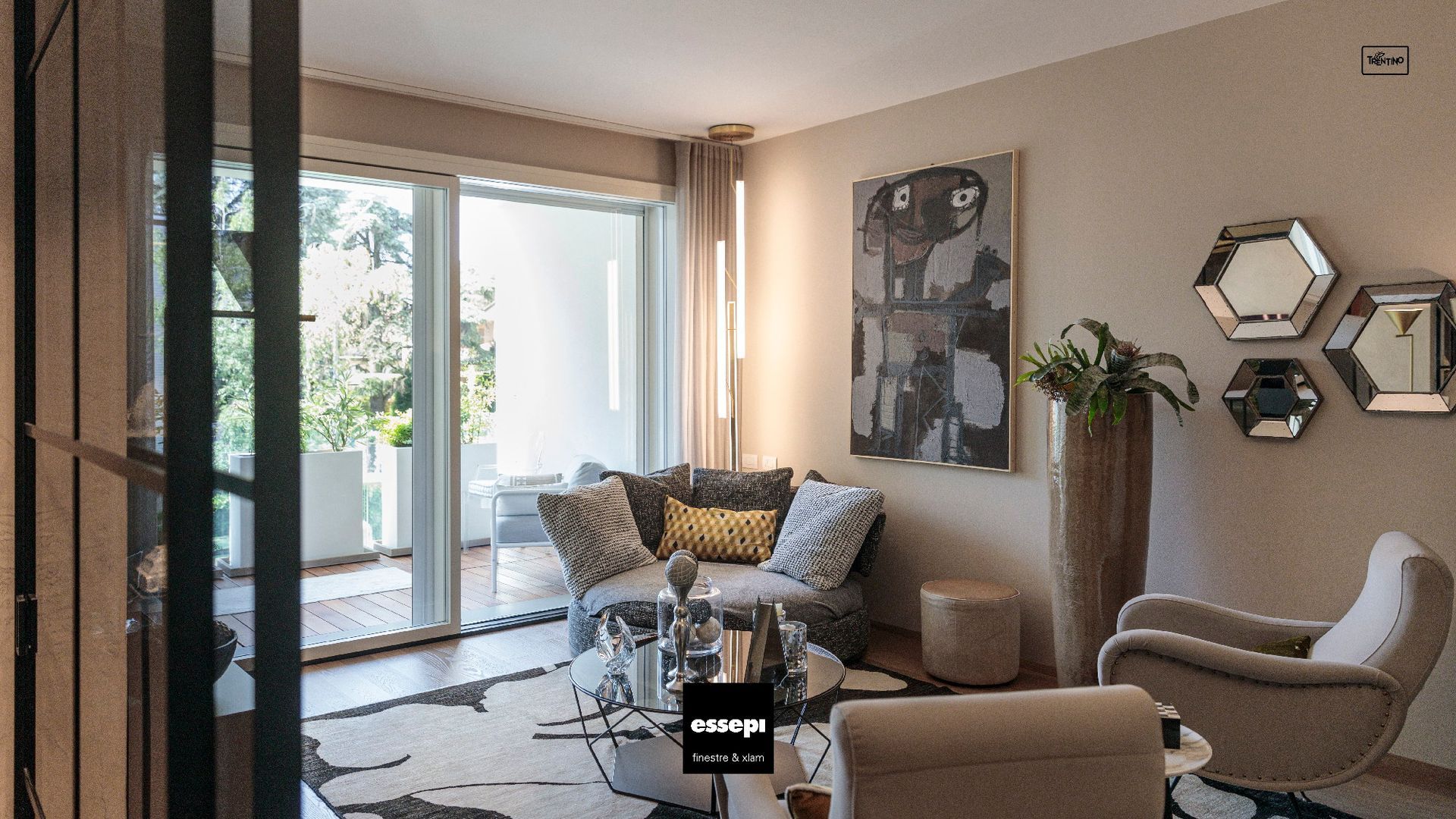 Soggiorno con divano grigio, opere d'arte moderna, specchi e porte scorrevoli in vetro che danno su un balcone.