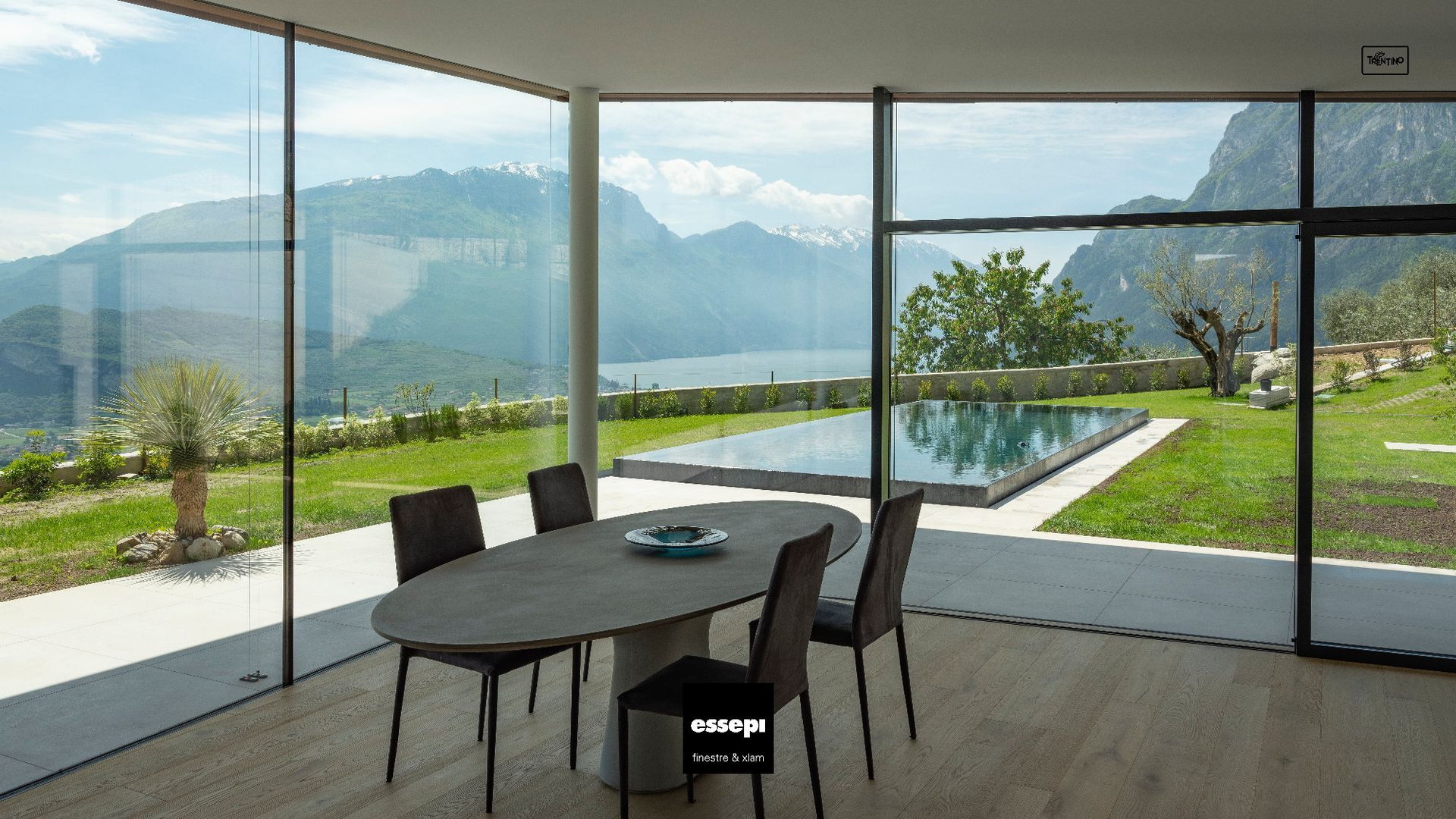Tavolo da pranzo in una moderna stanza con pareti in vetro e vista sulla piscina, sul giardino e sulle montagne.