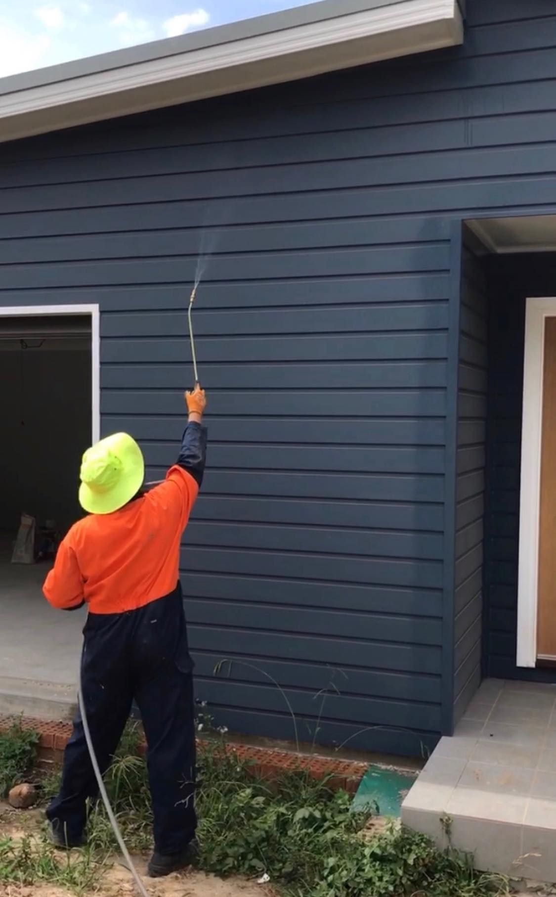 A Man is Spraying a Blue House With a Hose — City Coast Pest Solutions In Wollongong, NSW