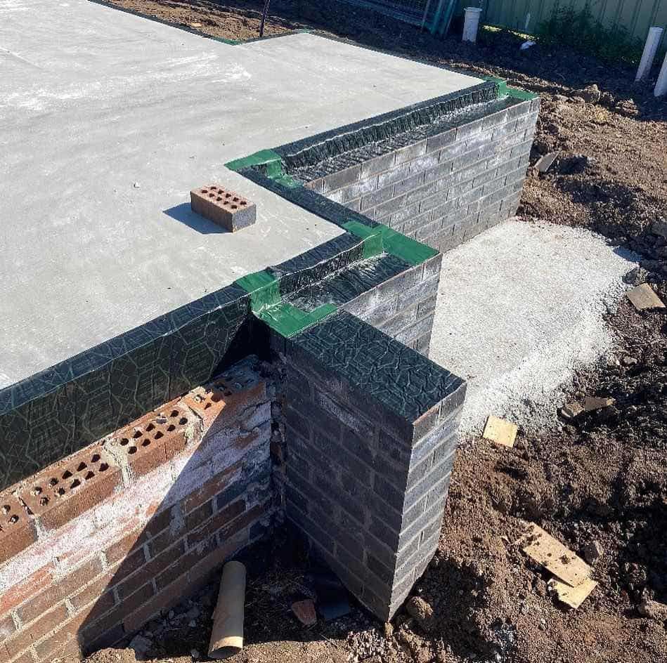 A Brick Wall is Being Built Next to a Concrete Slab — City Coast Pest Solutions In Wollongong, NSW