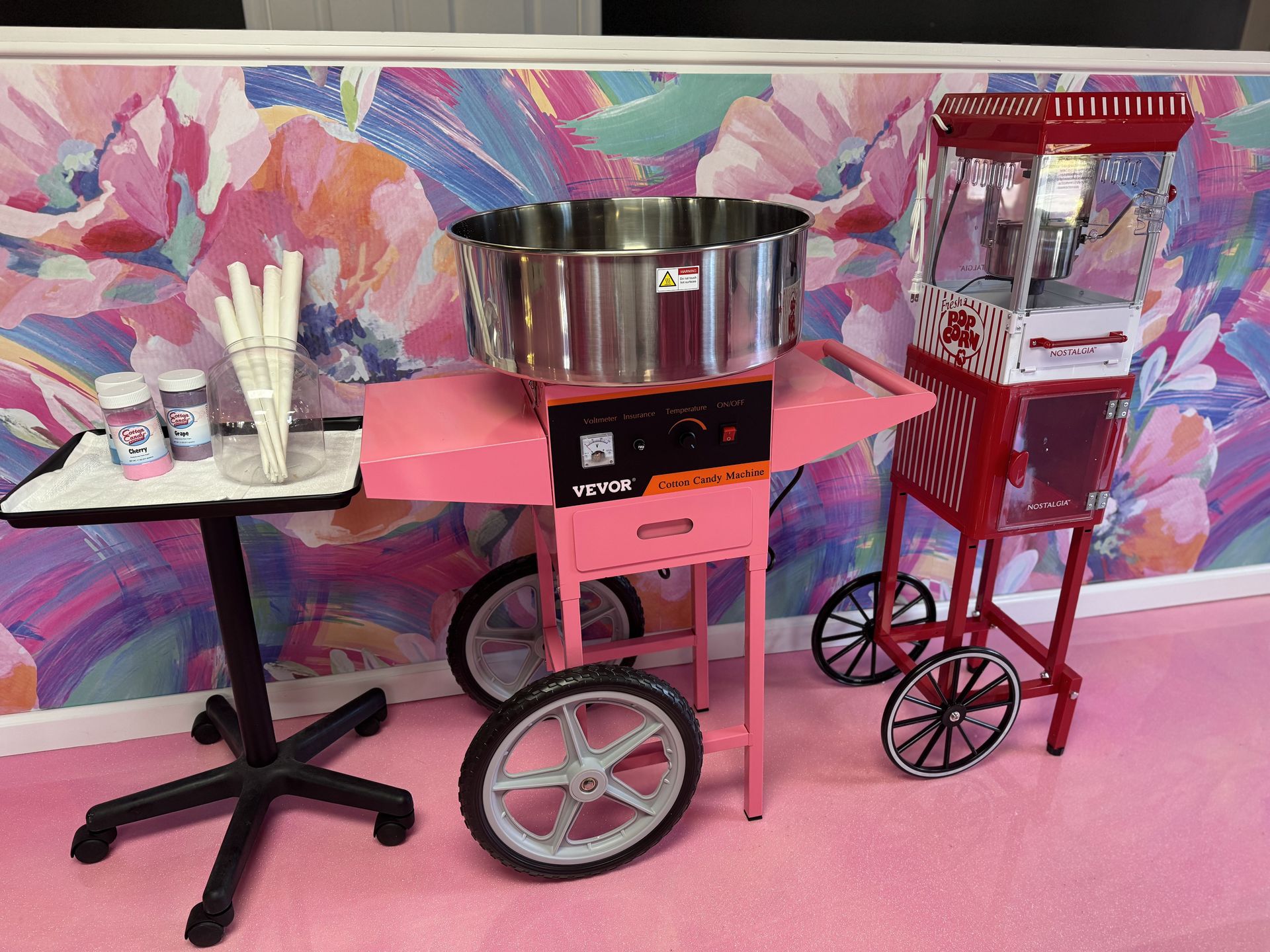 A pink cotton candy machine and a red popcorn machine are sitting next to each other in a room.