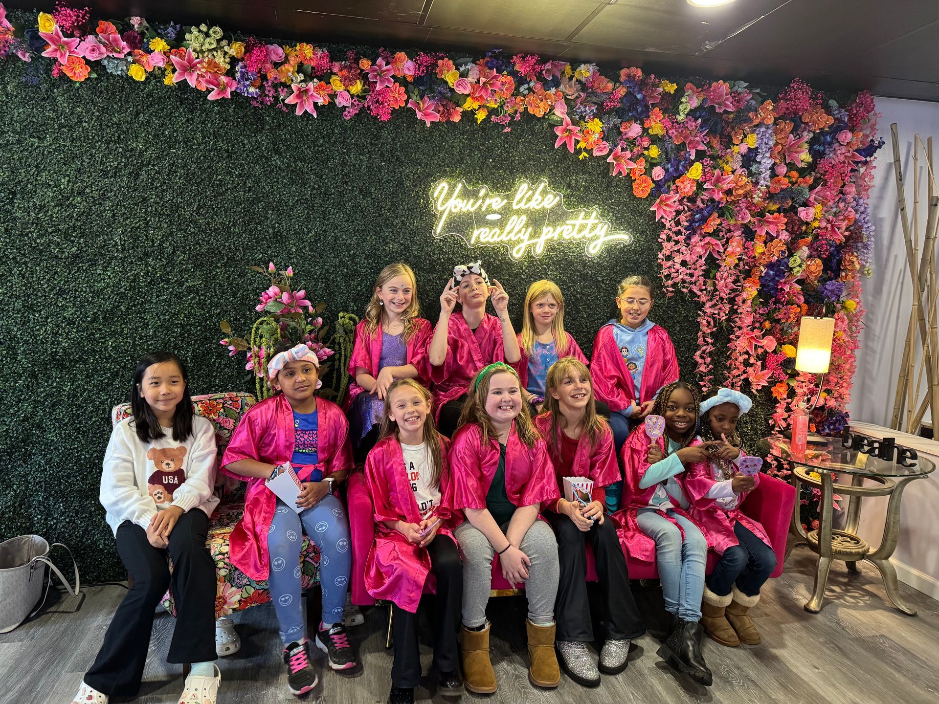 A group of young girls are posing for a picture in front of a flower wall.