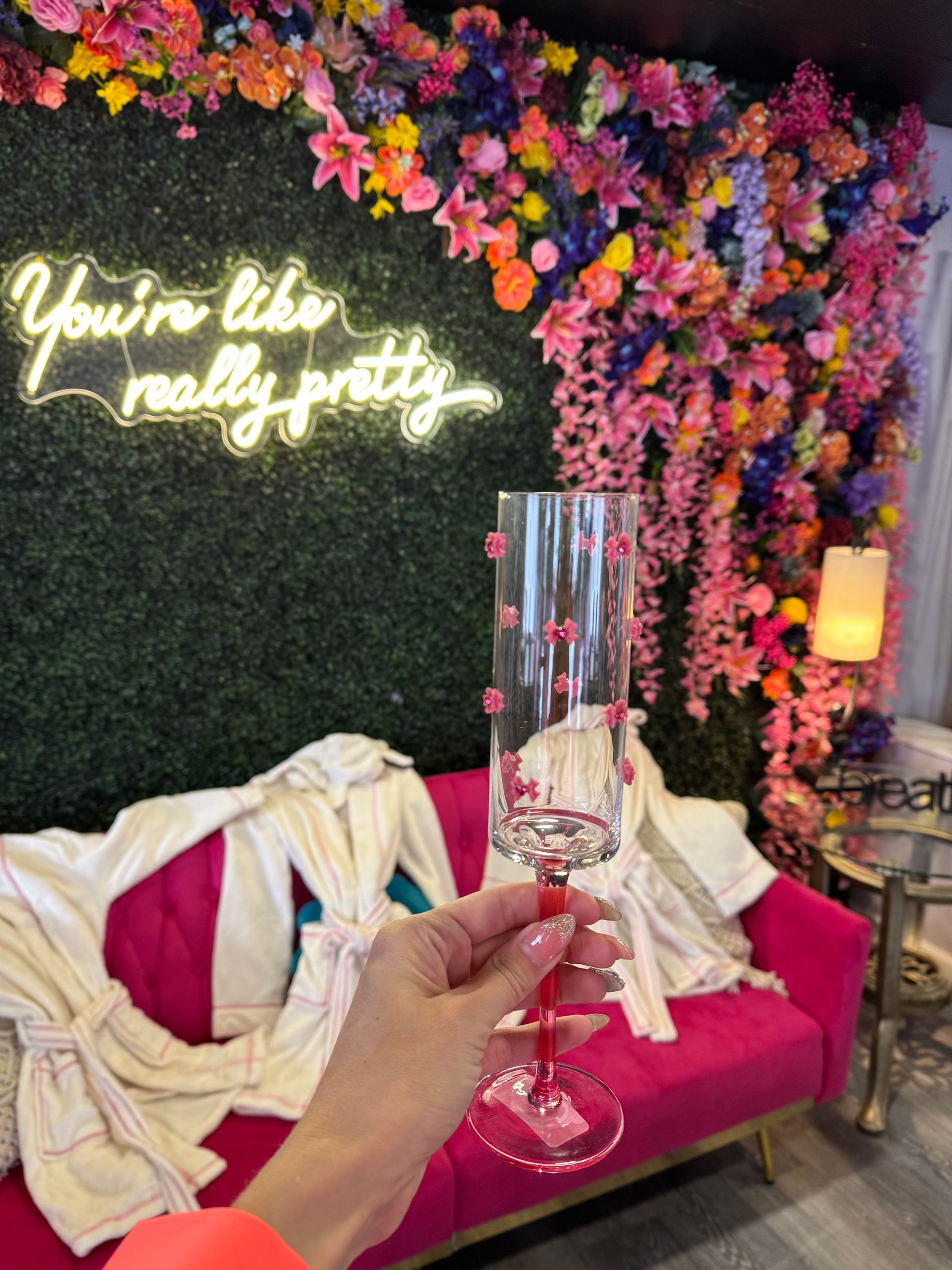 A person is holding a champagne glass in front of a neon sign that says you 're like really pretty.