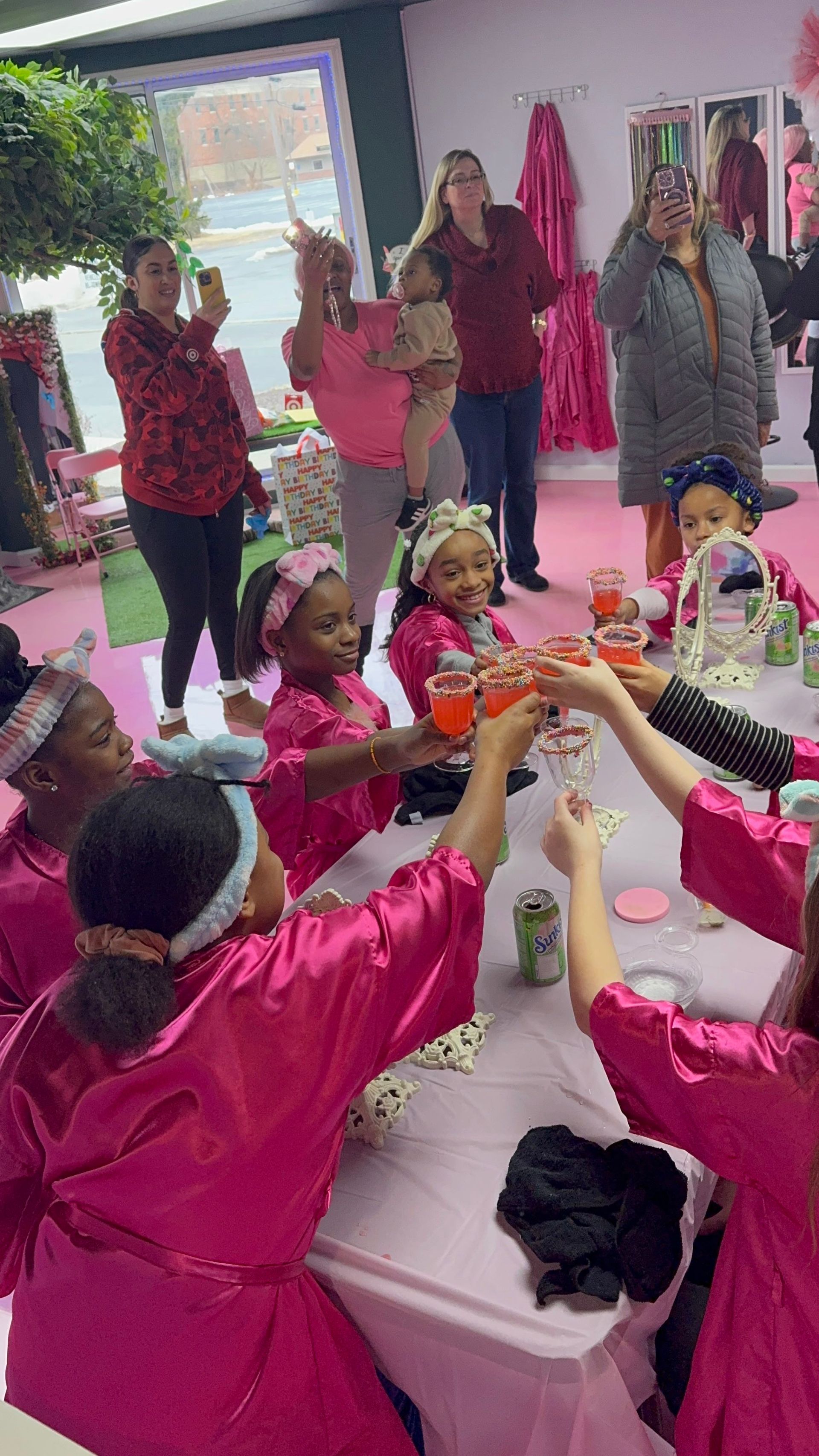 A group of young girls are sitting at a table toasting with drinks.
