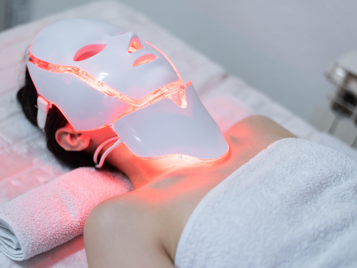 A woman is laying on a bed with a led mask on her face. A woman is laying on a bed with a led mask on her face.