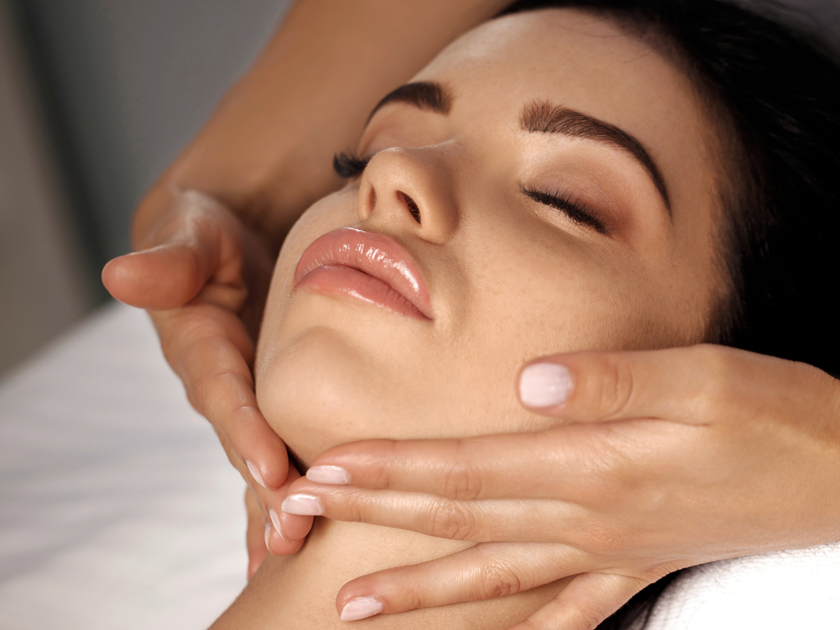 Woman receiving facial massage, eyes closed, hands on face and neck.