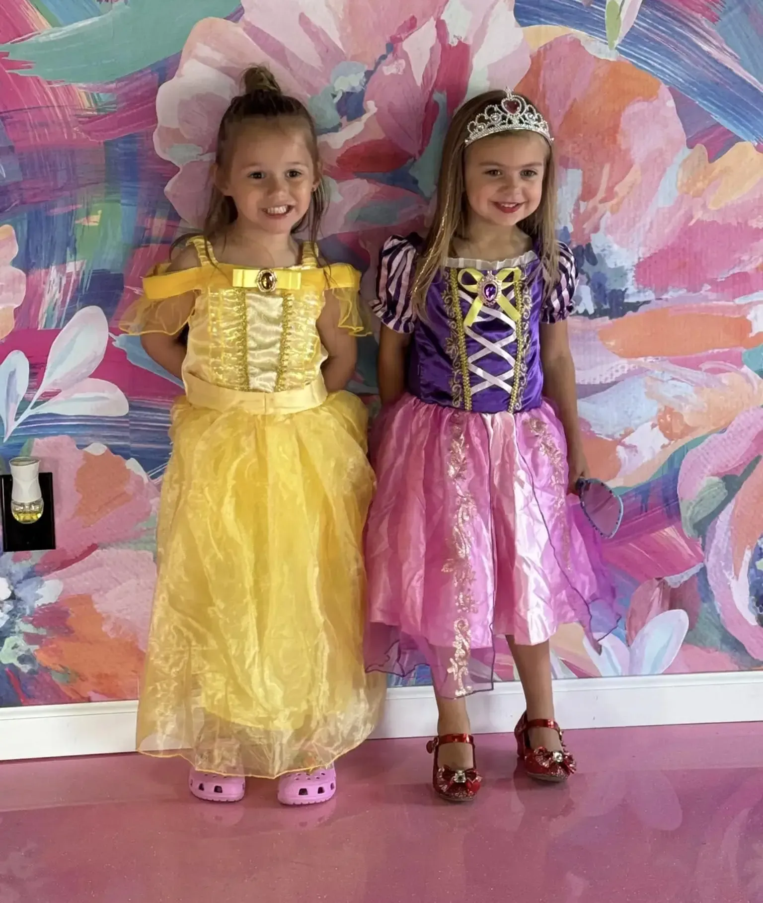 Two little girls in princess costumes are standing next to each other.