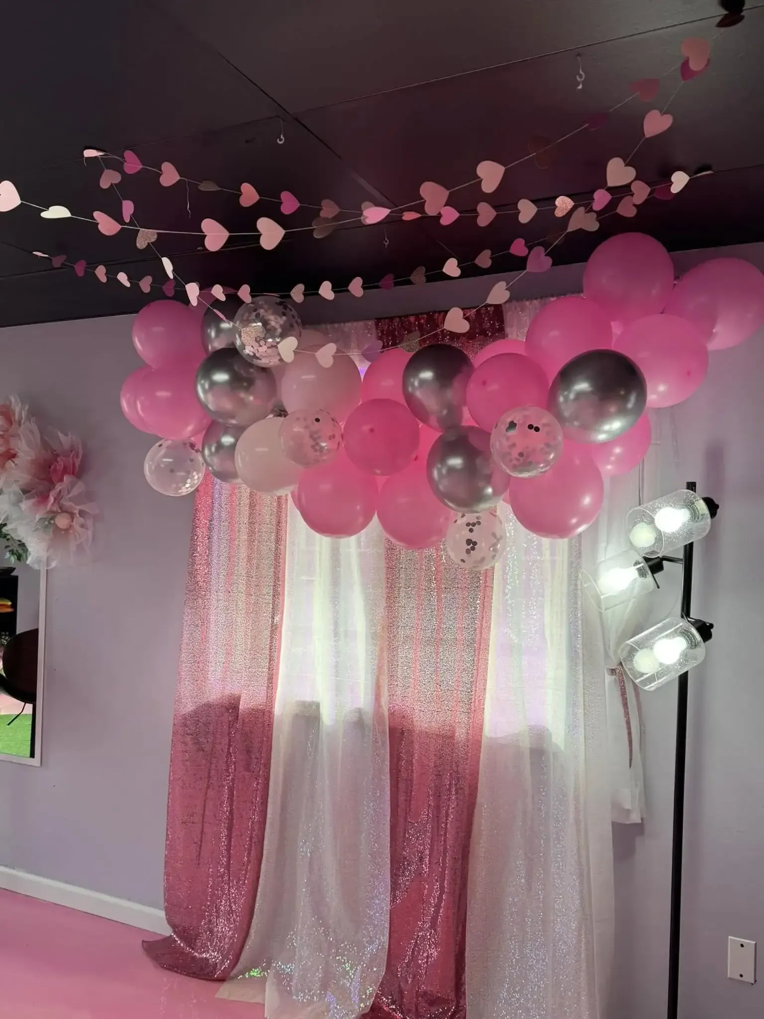 A room decorated with pink and silver balloons and hearts hanging from the ceiling.