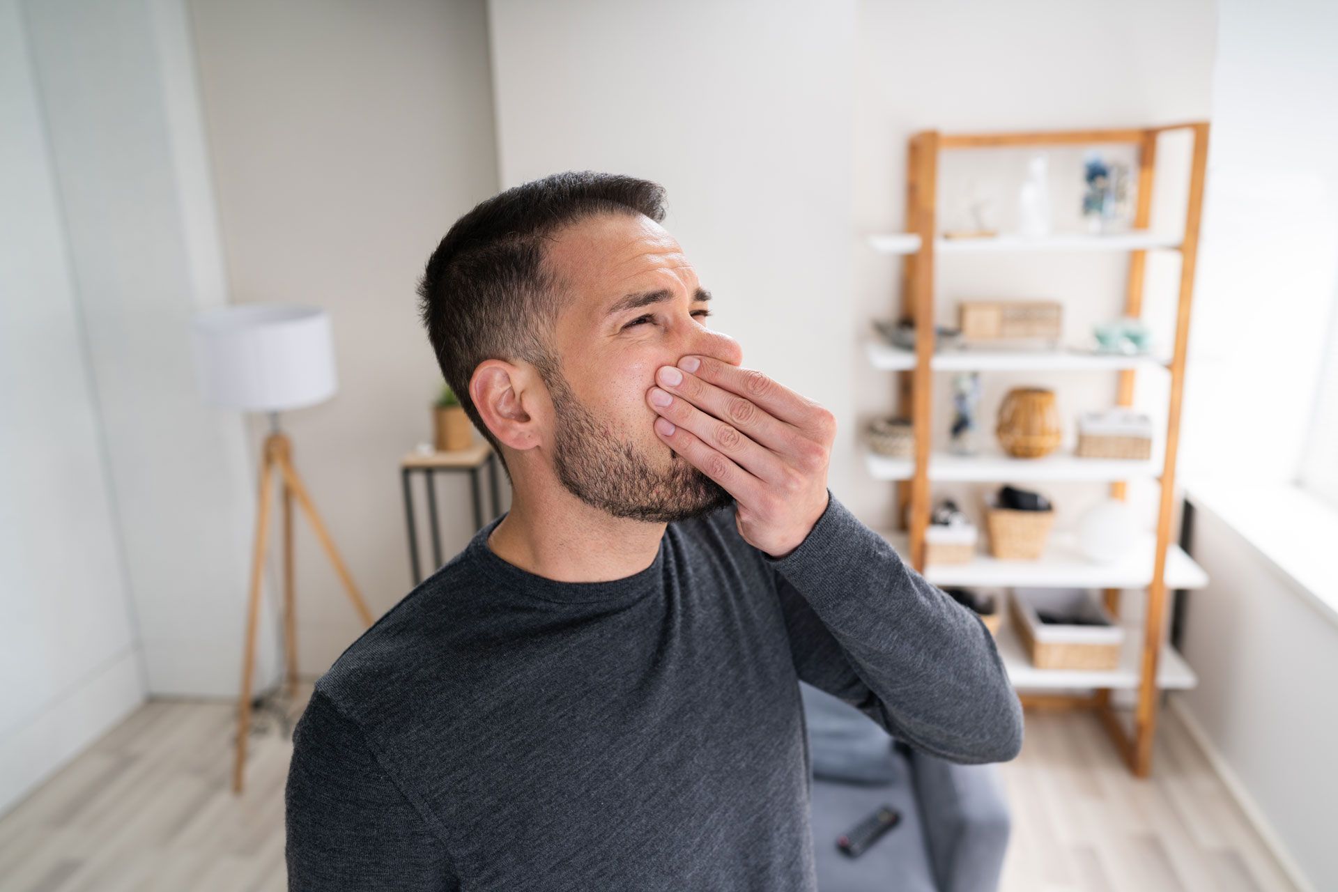 A man is covering his mouth with his hand in a living room.