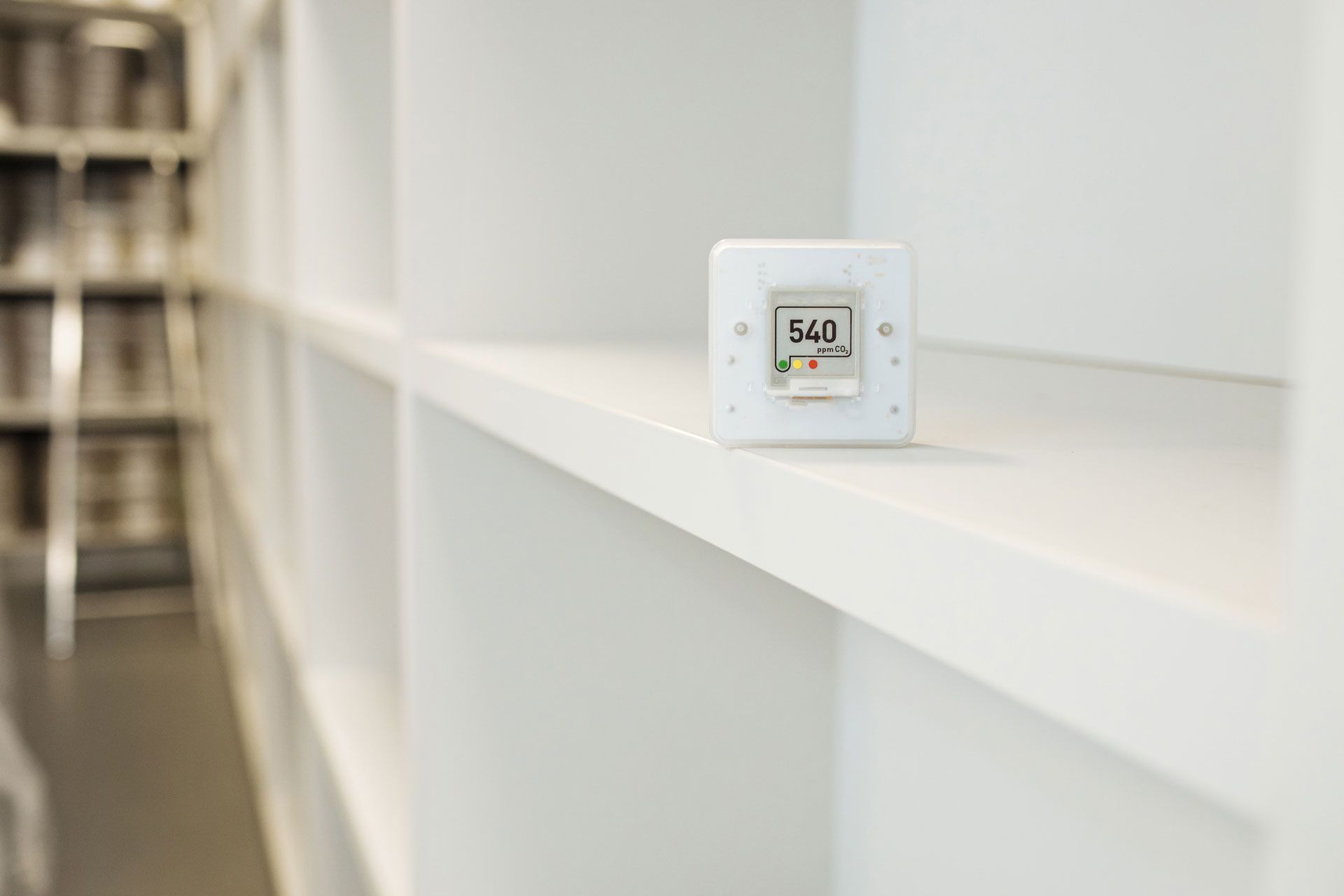 A white thermostat is sitting on a white shelf in a library.